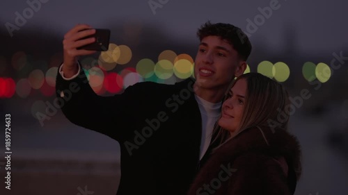 A young couple takes a selfie in Paris France at night The city lights create a bokeh background as the couple embraces and captures memories with a smartphone camera.
