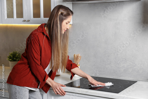 Woman wiping cooktop with paper towel in kitchen, space for text
