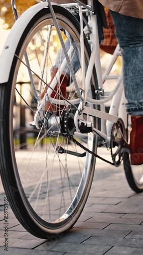 Back view of legs of unknown female who riding bike by city square. Autumn sunny day. Low angle tracking shot. Close up, slow motion