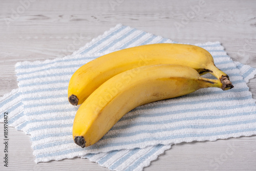 Yellow bananas placed on a blue and white striped cloth on a wooden table
