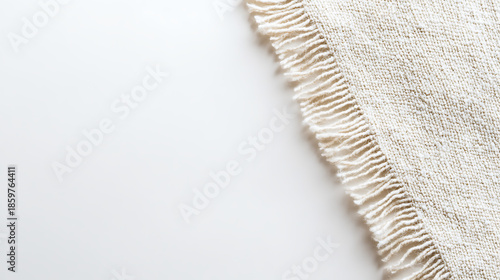 A textured, neutral-toned fabric with fringe edges placed on a clean, white background, emphasizing simplicity and subtle detail in a minimalist composition.
