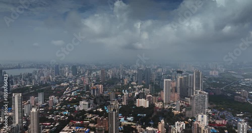 Cinematic aerial view of the Mumbai city skyline during the monsoon season, with dramatic clouds creating a moody and atmospheric backdrop.