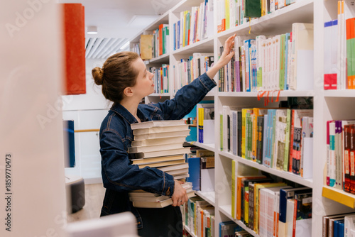 Wallpaper Mural woman is sitting at shelves in library, student is choosing book. library is filled with books. education, scientific work. university lecturer. young Caucasian woman is getting education. Torontodigital.ca