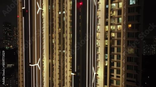 An aerial view of Mumbai's high-rise buildings and beautiful nightlights. The sky is cloudy, and there is medium traffic on the road. The cityscape is filled with modern illuminated buildings.