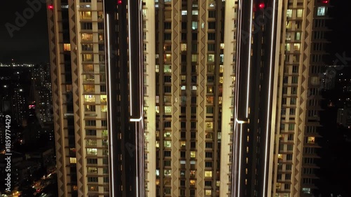 An aerial view of Mumbai's high-rise buildings and beautiful nightlights. The sky is cloudy, and there is medium traffic on the road. The cityscape is filled with modern illuminated buildings.