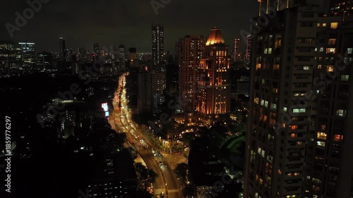 An aerial view of Mumbai's high-rise buildings and beautiful nightlights. The sky is cloudy, and there is medium traffic on the road. The cityscape is filled with modern illuminated buildings.