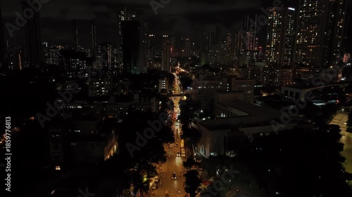 An aerial view of Mumbai's high-rise buildings and beautiful nightlights. The sky is cloudy, and there is medium traffic on the road. The cityscape is filled with modern illuminated buildings.