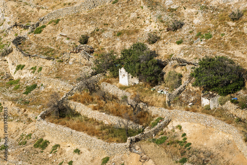 Historic hillside scene in Ano Syros, Greece, featuring terraced stone walls and a mix of preserved and ruined structures