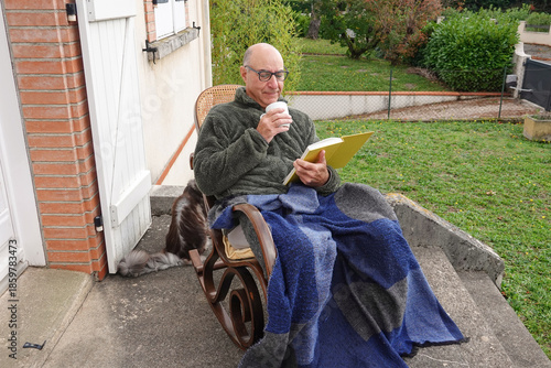A person relaxes outside on a chair with a drink and a book