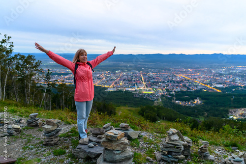 Joyful woman embraces the view from a mountain top overlooking a vibrant city at twilight