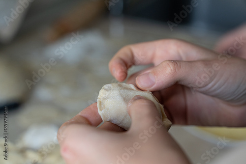 Close-up of hands carefully shaping dumpling dough with a braided edge. Homemade cooking process with selective focus, showing texture, tradition, and cooking at home atmosphere.