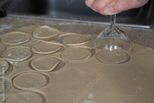 Perfectly cut dough circles dusted with flour on counter beside glass cutter, selective focus captures texture in cooking at home dumpling preparation process.