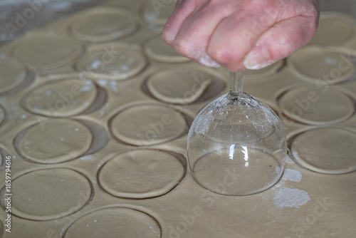 Perfectly cut dough circles dusted with flour on counter beside glass cutter, selective focus captures texture in cooking at home dumpling preparation process.
