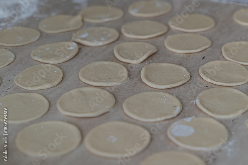 Symmetrical pattern of cut dough circles scattered with flour on work surface, selective focus emphasizes texture in cooking at home dumpling making tradition