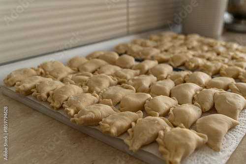 Cluster of handmade dumplings with pleated edges on paper towel, selective focus highlights texture amid cooking at home scene with scattered dough in background