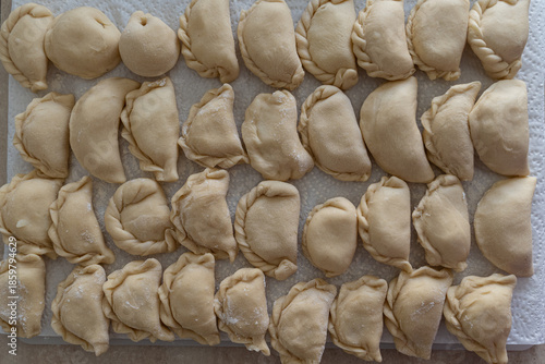 Cluster of handmade dumplings with pleated edges on paper towel, selective focus highlights texture amid cooking at home scene with scattered dough in background