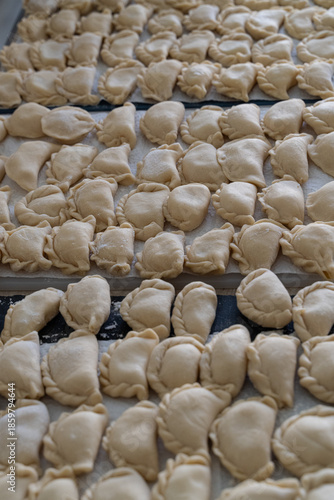 Cluster of handmade dumplings with pleated edges on paper towel, selective focus highlights texture amid cooking at home scene with scattered dough in background
