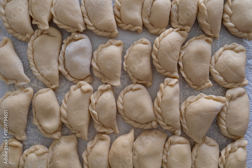 Cluster of handmade dumplings with pleated edges on paper towel, selective focus highlights texture amid cooking at home scene with scattered dough in background