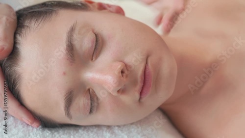 Closeup of young woman with closed eyes receiving gentle facial massage for relaxation and skincare treatment at spa center promoting beauty wellness and rejuvenation