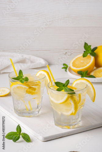 Refreshing drinks with lemon slices and mint leaves on a white surface in a bright setting and fresh fruits in the background