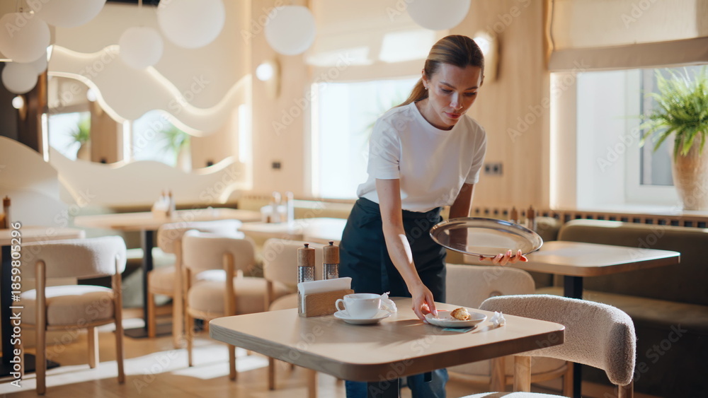 Fototapeta premium Cafe waitress cleaning table taking dishes after client. Girl staff working