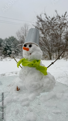 A real snowman made of snow, close-up, with a light green scarf outside
