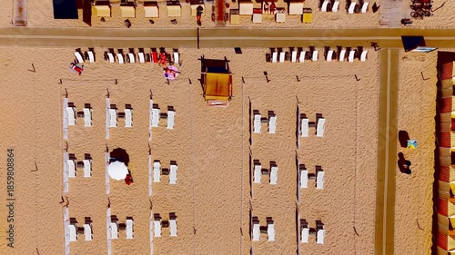Top down aerial rise revealing beach cabanas and sun loungers on sandy beach