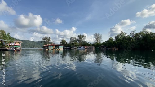 Traditional Bajo tribe stilt houses built over crystal clear sea water. Scenic coastal village of sea gypsies with green hills and blue sky reflections in Central Sulawesi, Indonesia.