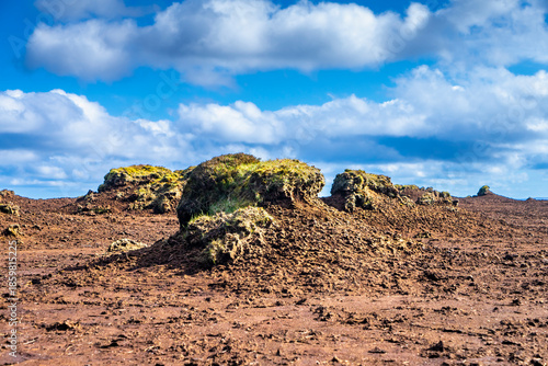 Eroded peatland landscape with exposed dark soil and isolated peat ‘islands’ under a bright blue sky