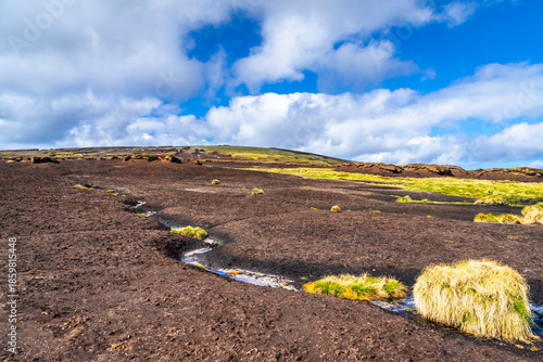 Eroded peatland landscape with exposed dark soil and isolated peat ‘islands’ under a bright blue sky