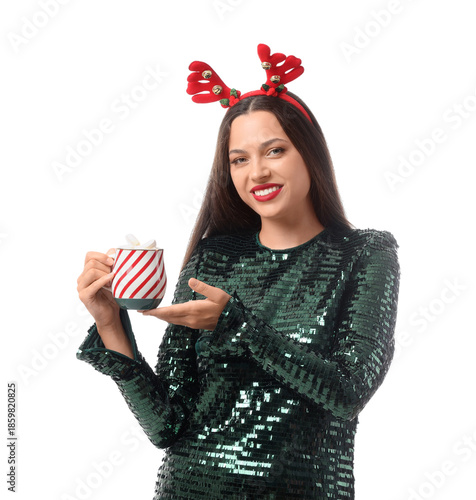 Happy young woman in party dress and reindeer horns holding cup of hot chocol...