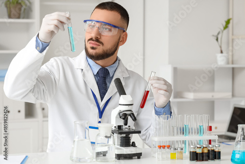 Male scientist with test tubes and microscope at table in laboratory