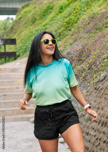 An athletic girl wearing black glasses smiles as she warms up to go for a run on a sunny morning.