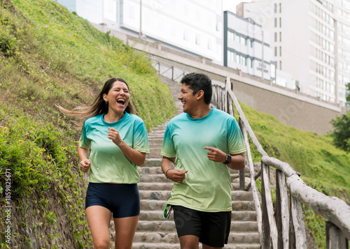 Multiracial, athletic couple running and smiling while training outdoors on a sunny morning.