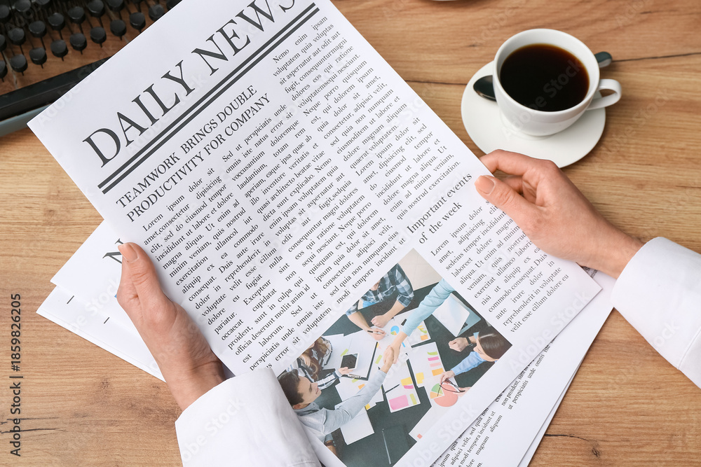 Obraz premium Female hand holding newspaper and cup of coffee on wooden background