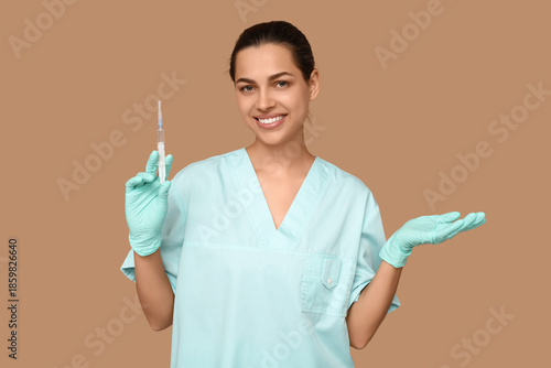 Portrait of female doctor with syringe showing something on beige background