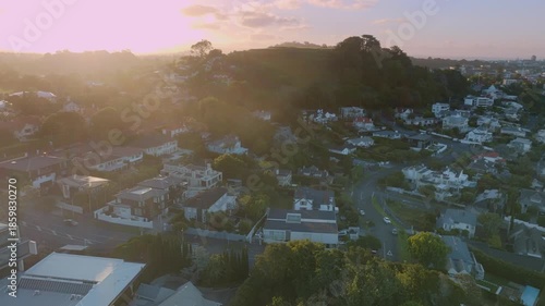 Aerial view of Remuera, Auckland, New Zealand, at sunset. The sun shines over the houses and trees of the city, creating a warm and inviting scene. The scene captures the beauty of urban life.