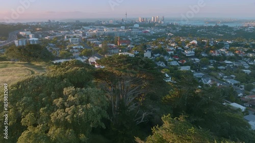 Aerial view of Auckland, New Zealand, showing the city skyline and residential areas. The scene captures the urban landscape and the natural beauty of the region.