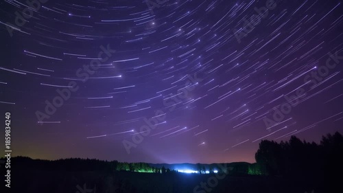 Mesmerizing long exposure captures the ethereal star trails painting a vibrant, purple-hued night sky, illustrating the cosmic journey above a tranquil, silhouetted landscape
