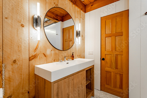 Fotografía Rustic modern bathroom with wooden vanity, round mirror and warm lighting in coz