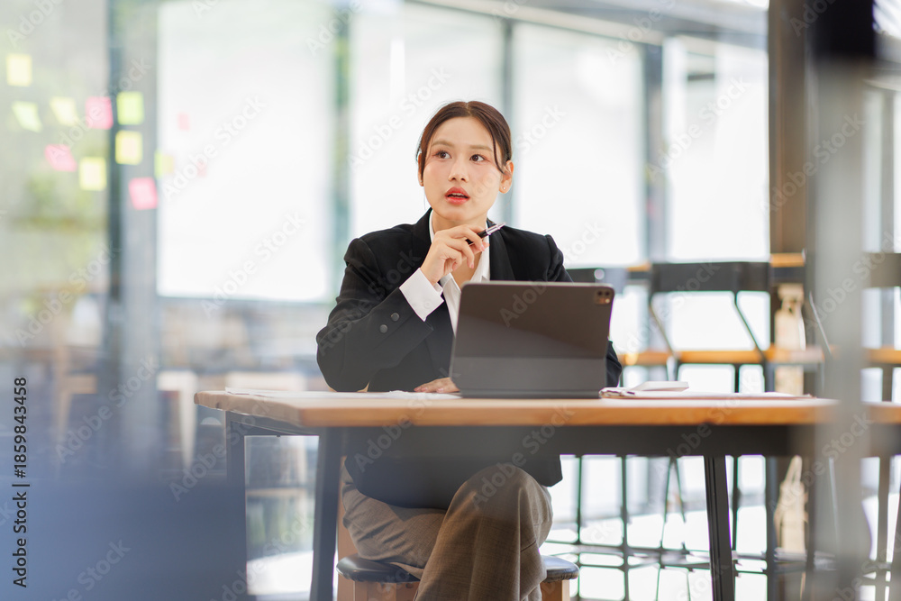 Fototapeta premium Portrait of a confident and smiling Asian business woman working on tablet at her desk in a modern office. 