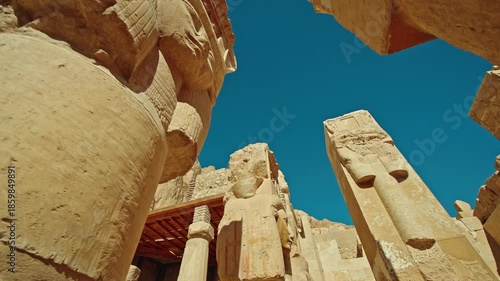 Low angle view of colossal ancient statue and massive stone columns at the Temple of Hatshepsut in Luxor, Egypt, highlighting monumental ancient Egyptian architecture