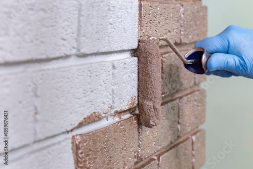 Person painting over a grey brick wall with rose gold metallic paint using a paint roller. Do it yourself home improvement concept.