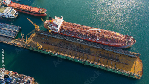 Detailed aerial shot of a rusty red ship hull in a dry dock being prepared for sandblasting and painting as part of the heavy maintenance process in a shipyard
