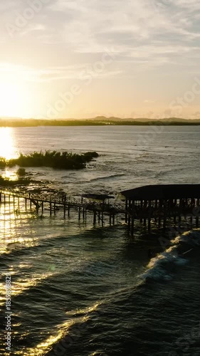 Golden sunset shines over pier and surfers in the ocean. Siargao, Philippines. Cloud 9 Surfing Area.