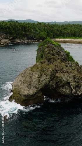 Aerial view of rock formation rises in the sea close to the coast with forest and sandy beach. Siargao, Philippines.