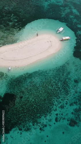 A small sand island is surrounded by turquoise sea with several boats anchored near the shore. Naked Island. Siargao, Philippines.