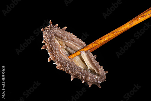 Raw sea cucumber trepang with chopsticks on black background © zhikun sun