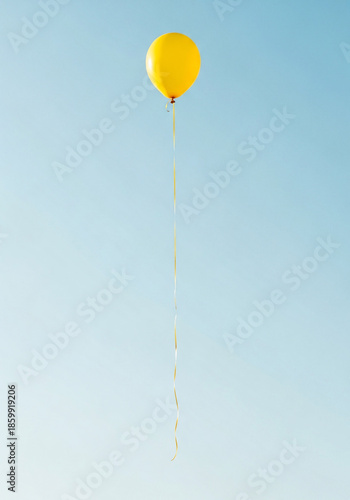 A solitary vibrant yellow balloon with a long ribbon floats high in a clear serene blue sky symbolizing joy.