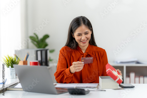 Fotografi Surprised Unboxing: Captivating scene of a woman, radiating joy as she unveils a surprise gift and a credit card